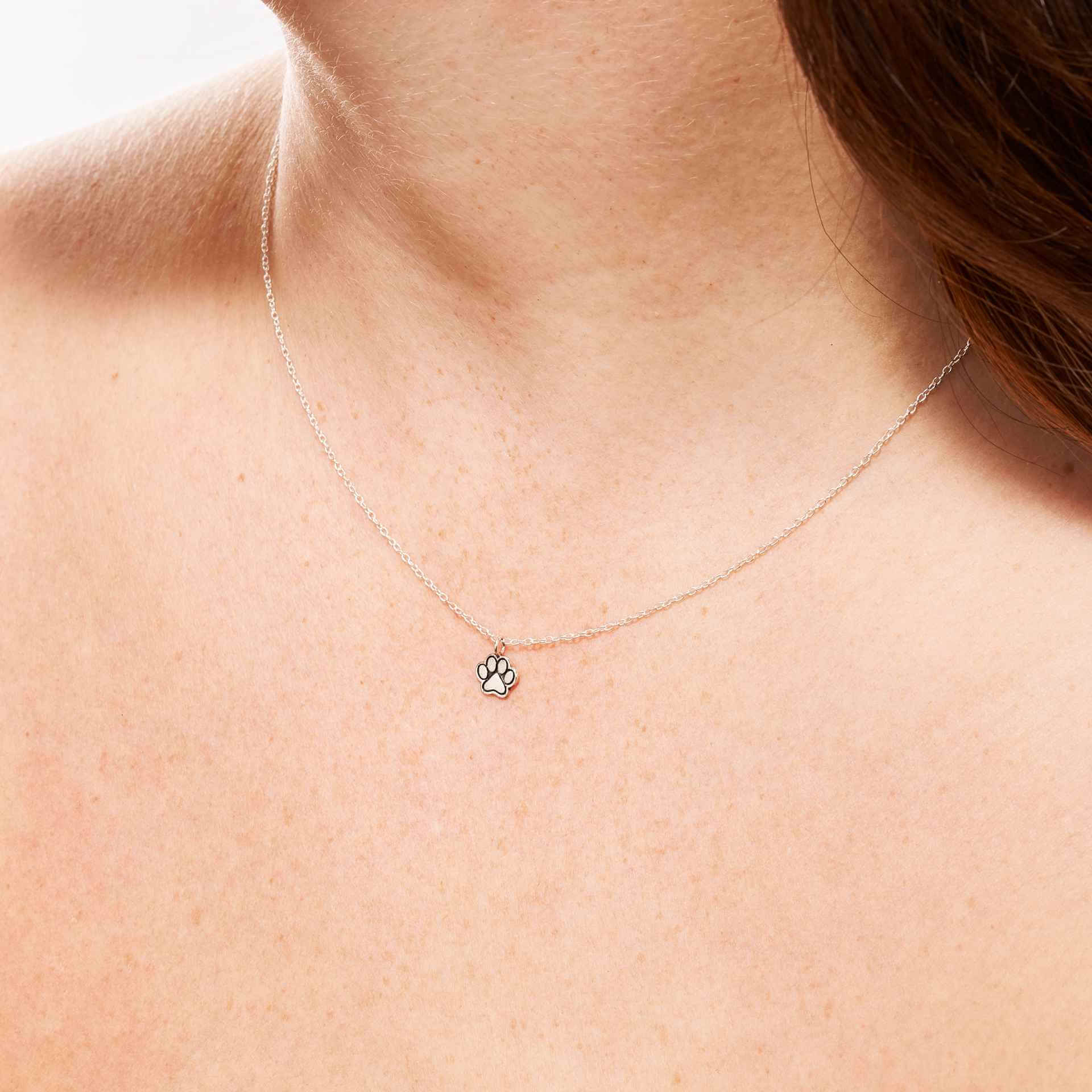 Paw print necklace silver shown worn close to the neckline, simple and subtle.