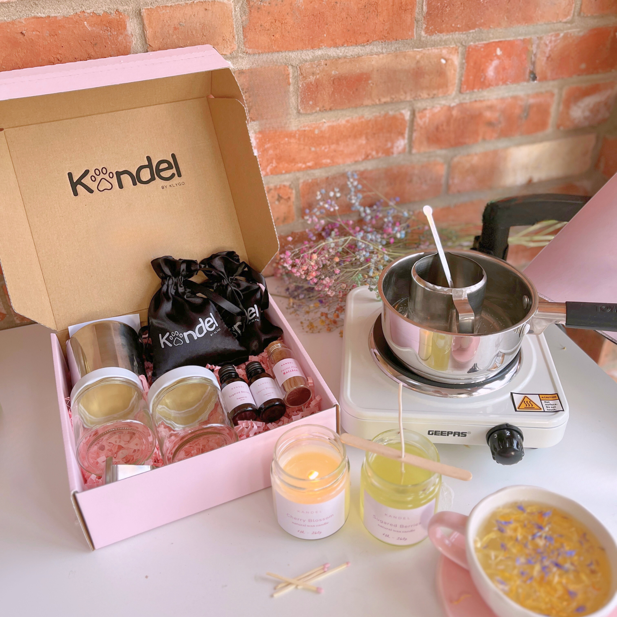 Flat lay of a candle-making kit with supplies to make two scented candles, including wax, wicks, fragrance oils, and candle containers. The scene features pink packaging in the background, creating a soft and inviting aesthetic.