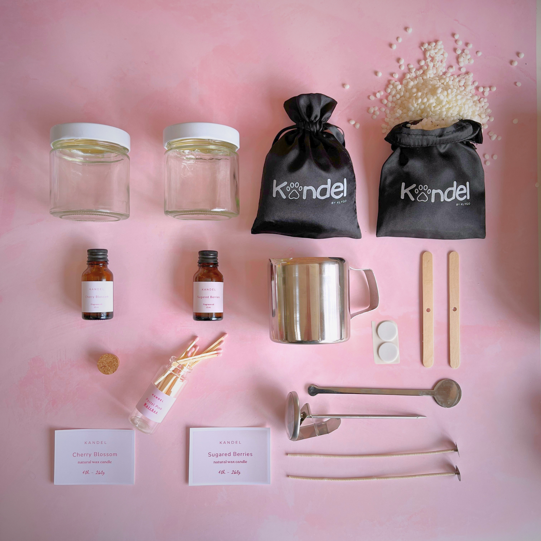 Image of a candle-making kit featuring wax flakes, wicks, fragrance oils, candle containers, a thermometer, and a mixing spoon, all neatly organized on a flat surface.