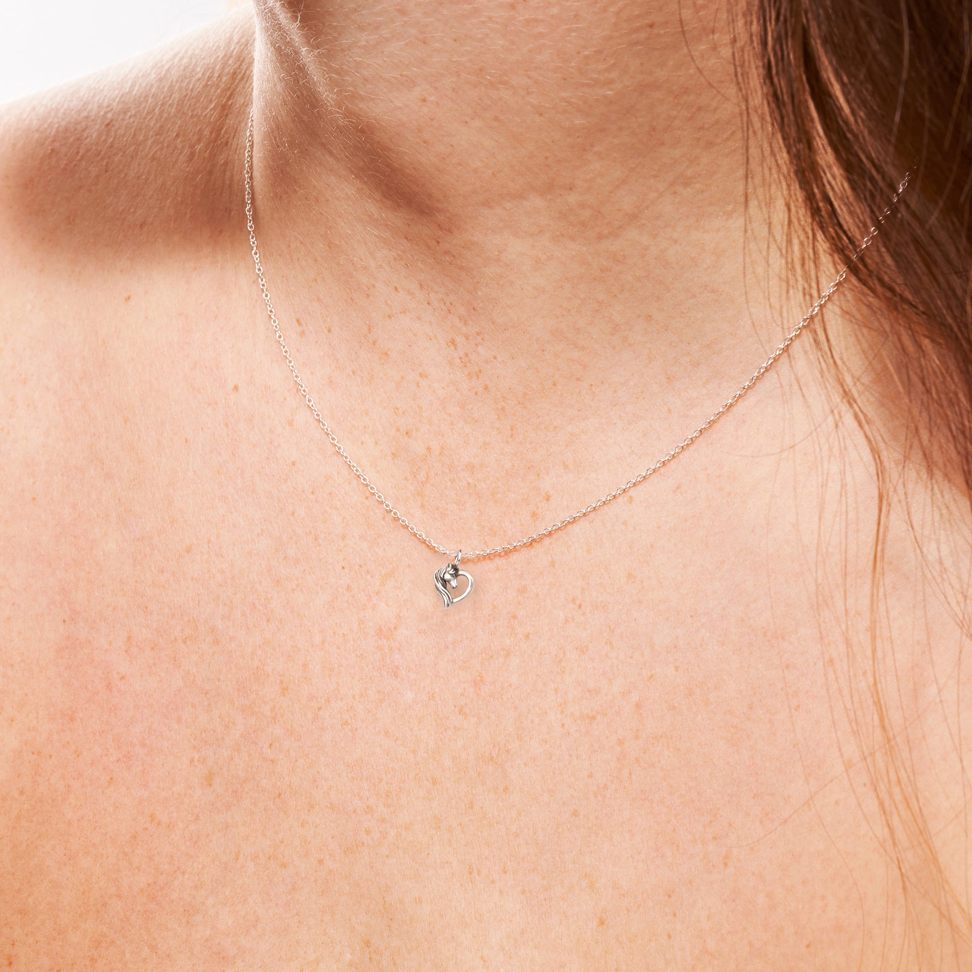 Horse necklace in sterling silver worn on bare skin, showing delicate chain and heart detail.